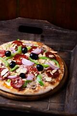 Pizza with chorizo ​​sausage, mozzarella cheese, green pepper and black olives. Rustic wooden background. Soft focus.	