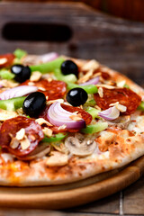 Pizza with chorizo ​​sausage, mozzarella cheese, green pepper and black olives. Rustic wooden background. Soft focus.	