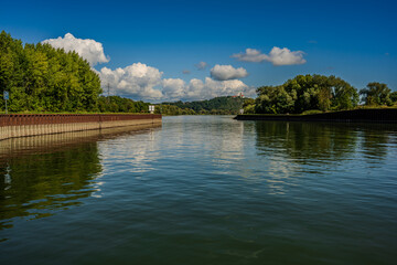 Fototapeta premium Ruhe am Fluss mit reflektierenden Wolken und grünen Uferbäumen bei klarem Wetter