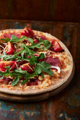 Pizza with ham, salami, tomatoes and mozzarella cheese. Rustic wooden background. Soft focus. Close up.	