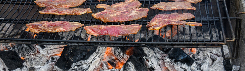 Closeup of Korean style beef cooking on an outdoor barbeque grill with hot coals below, as part of...
