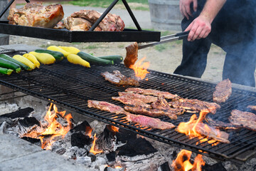 Korean style beef cooking on an outdoor barbeque grill with hot coal below, chef using tongs to...