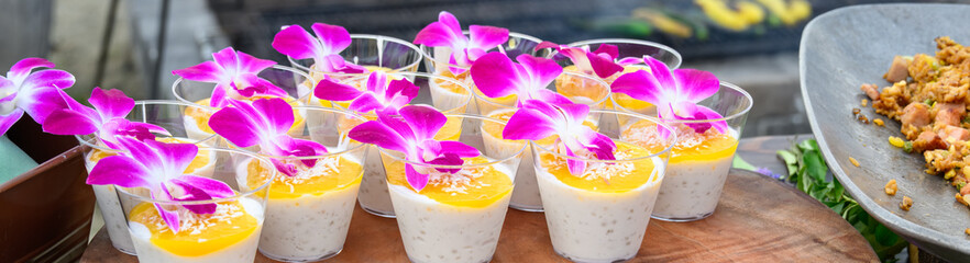 Tropical tapioca pudding mango sauce and coconut shavings topped with a purple orchid flower,...