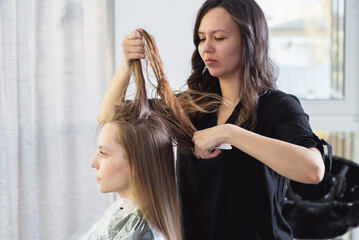 Fototapeta premium Close up of hairdressers hands drying long blond hair with blow dryer and round brush