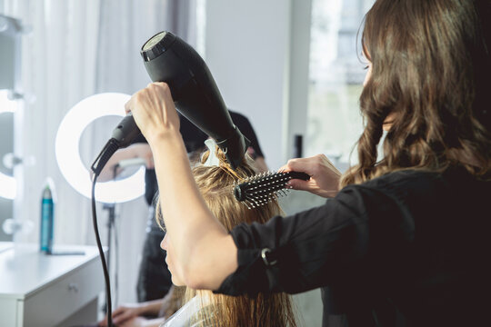 Close up of hairdressers hands drying long blond hair with blow dryer and round brush