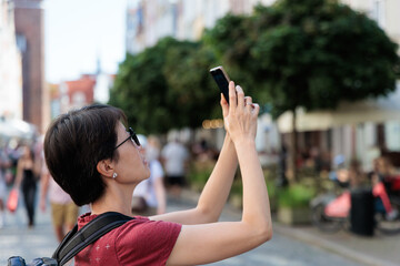 Woman with backpack taking photo on smartphone while exploring urban streets on a city sightseeing...