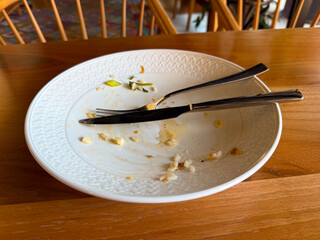 Empty plate with fork and knife on wooden table after meal. Dining experience, lifestyle, and hospitality representing daily habit, culture, and consumption.