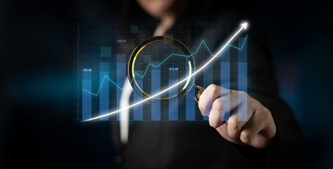 A business professional evaluates financial data using a magnifying glass on graphs in a modern office setting, highlighting growth and analysis trends. Impute