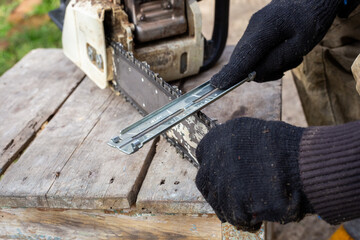 Close-up of male hands with a sharpener sharpening a chainsaw chain on a wooden workbench, in order...