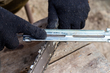 Close-up of male hands with a sharpener sharpening a chainsaw chain on a wooden workbench, in order to improve its performance.