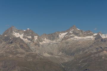 Mountain peak with snow cap and clear blue sky over rugged terrain during daytime