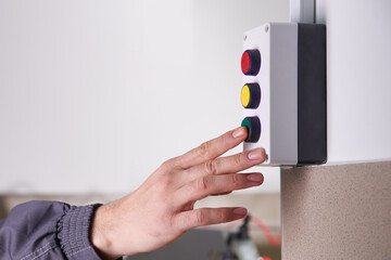 Worker pushing green button operating a machine in a factory, close up of hand