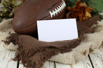Blank white horizontal card mockup on fabric backing with rugby ball and dried maple leaves, soft natural light.