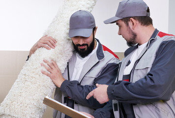 Two men taking away big carpet for cleaning service