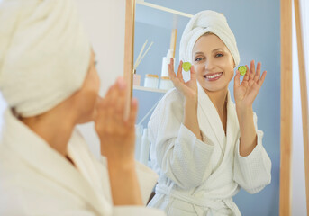 Smiling woman holding two cucumber slices near face, going to apply on eyes for skin moisturising,...