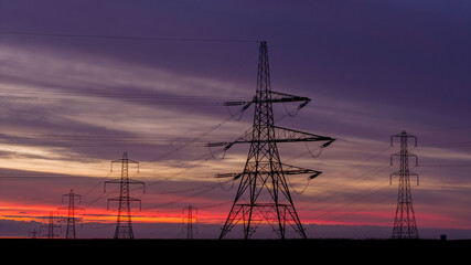 Electricity Pylons at Sunrise with Vibrant Sky in Rural Landscape