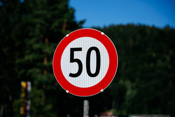Speed limit sign with 50 in red circle against green forest background