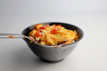 A spoon scooping up omelette with carrot, with a black ceramic bowl in the background.