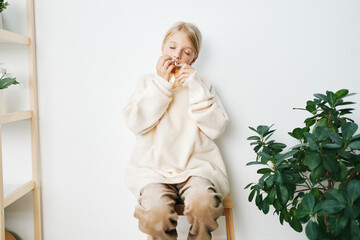A person sits on a small wooden stool wearing a fluffy cream sweater, savoring a snack in a bright,...