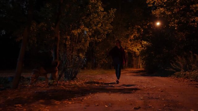 Young woman is walking her dog on a night suburban street