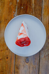 Indulgent slice of creamy cake topped with vibrant strawberry sauce on a rustic wooden table