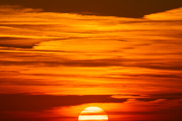 A blazing sun sinks beneath glowing clouds, casting a fiery palette of orange, red, and gold across...