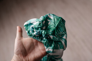 Hand holding a green scrunchie with tropical leaf pattern.