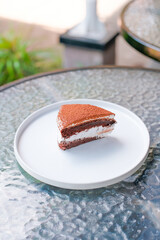 Indulge in delicious chocolate cake slice with creamy layers on a bright white plate outdoors