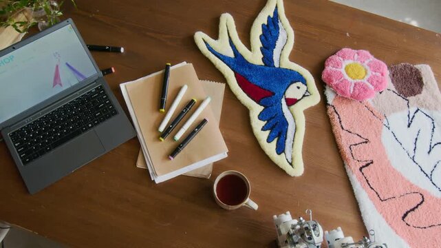 Top view shot of laptop and colorful handmade rugs on wooden table in rug tufting workshop, small business concept, copy space