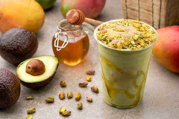 Avocado Smoothie with Pistachios and a Drizzle of Honey in plastic cup side view of summer drink