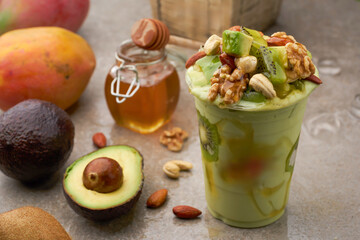 Creamy Avocado Smoothie with Kiwi, Mixed Nuts, and Honey Drizzle in plastic cup side view of summer...