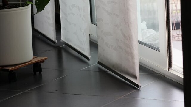 White vertical blinds moving gently in the wind from an open sliding door