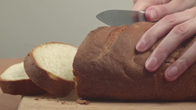 Close-up of young woman slicing fresh white bread with a kitchen knife on a cutting board in her kitchen, recorded with ambient sound.