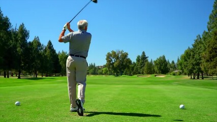 Senior white male golfer shows proper swing technique on a sunny day at a beautiful golf course. Lush green surroundings enhance the activity and focus on improving skills