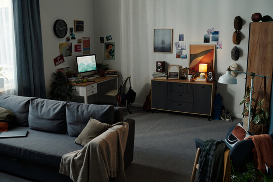Empty living room with computer monitor on desk displaying digital content suggesting gadget addiction, modern workspace setup indicating prolonged screen usage, no people visible