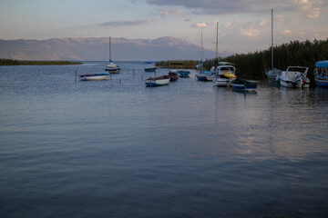collection of small fishing boats and sailboats are moored on a calm lake with mountains in the...