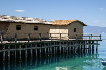a rustic stilt village on a tranquil lake with traditional mud huts and thatched roofs. the wooden...