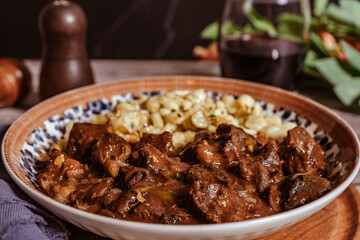 Delicious hungarian goulash with spaetzle and red wine being served on a plate