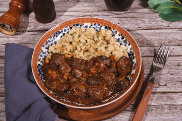 Delicious hungarian goulash with spaetzle, mushrooms and spices on rustic wooden table