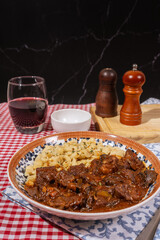 Delicious hungarian goulash with spaetzle and red wine on checkered tablecloth