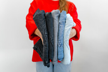 A woman in a red sweater holds a stack of colorful jeans against a white background. Clean, stylish...