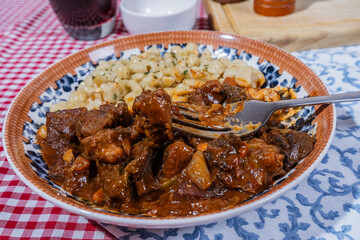 Fork lifting a piece of beef stew with spaetzle on the side, a hearty and flavorful meal