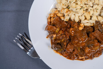 Delicious hungarian goulash with spaetzle on white plate resting on gray tablecloth with fork