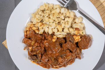 Delicious hungarian goulash with spaetzle garnished with parsley on white plate