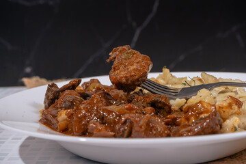 Fork lifting piece of beef from plate of goulash and spaetzle