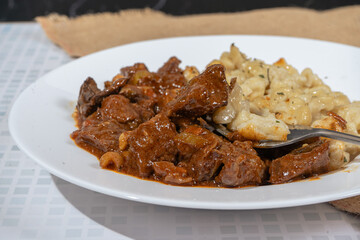 Fork lifting a bite of spaetzle from a plate of beef goulash