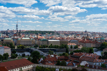 Fototapeta premium Panoramic cityscape featuring a river running through a historic European city under a bright blue sky with fluffy white clouds.