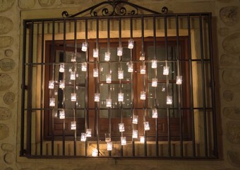 Window decorated with lit candles illuminating it, forming a heart in the darkness of the night.