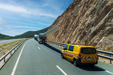 Special oversized transport carrying a wind turbine blade with pilot vehicle signaling hazard behind © M. Perfectti