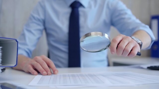 Businessman is carefully examining financial documents with a magnifying glass, highlighting the importance of thorough analysis in business. Audit and taxes